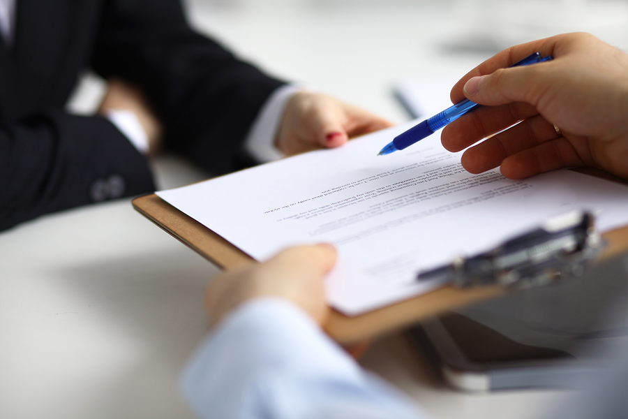 Close up of an executive hands holding a pen and indicating where to sign a contract at office.